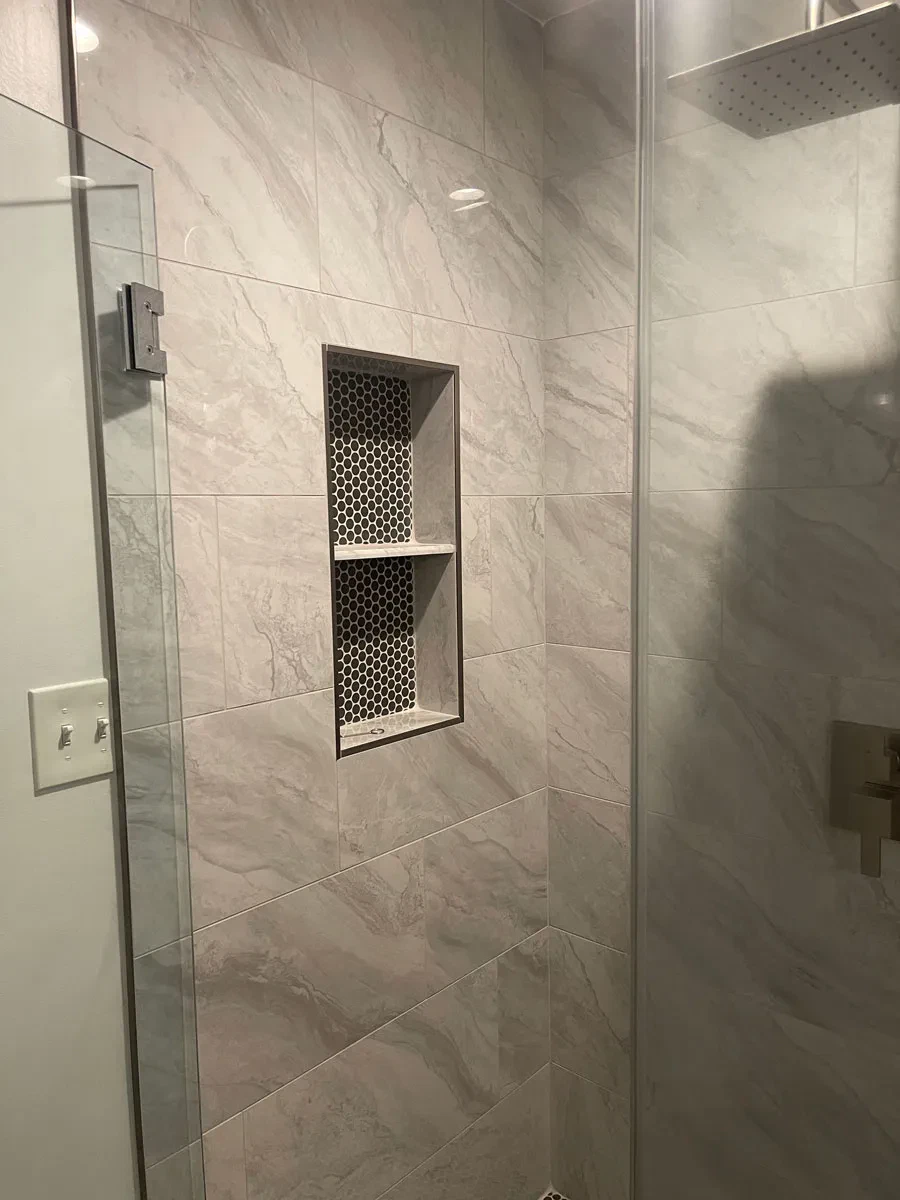 Modern marble tiled shower with glass door and shelf